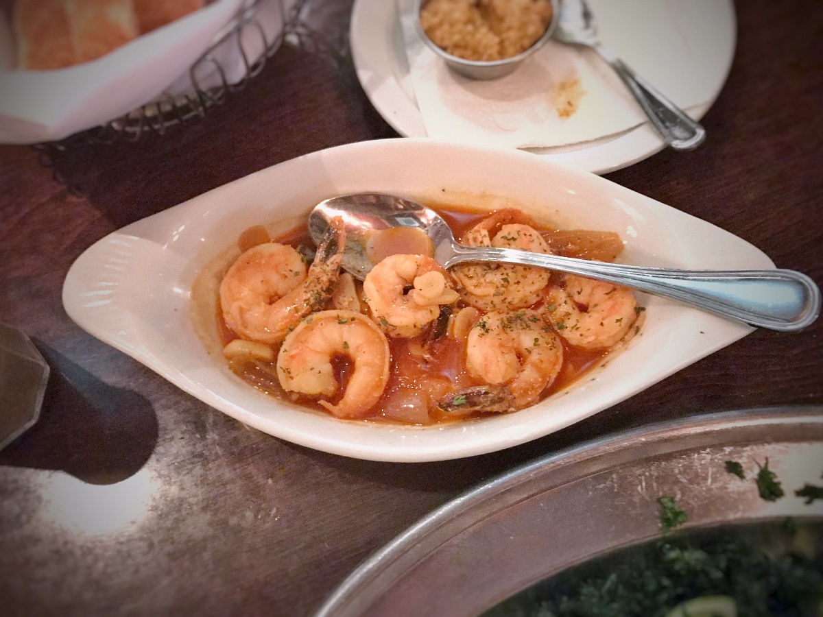 Un plato de camarones en salsa de ajo con una cuchara en la mesa del restaurante