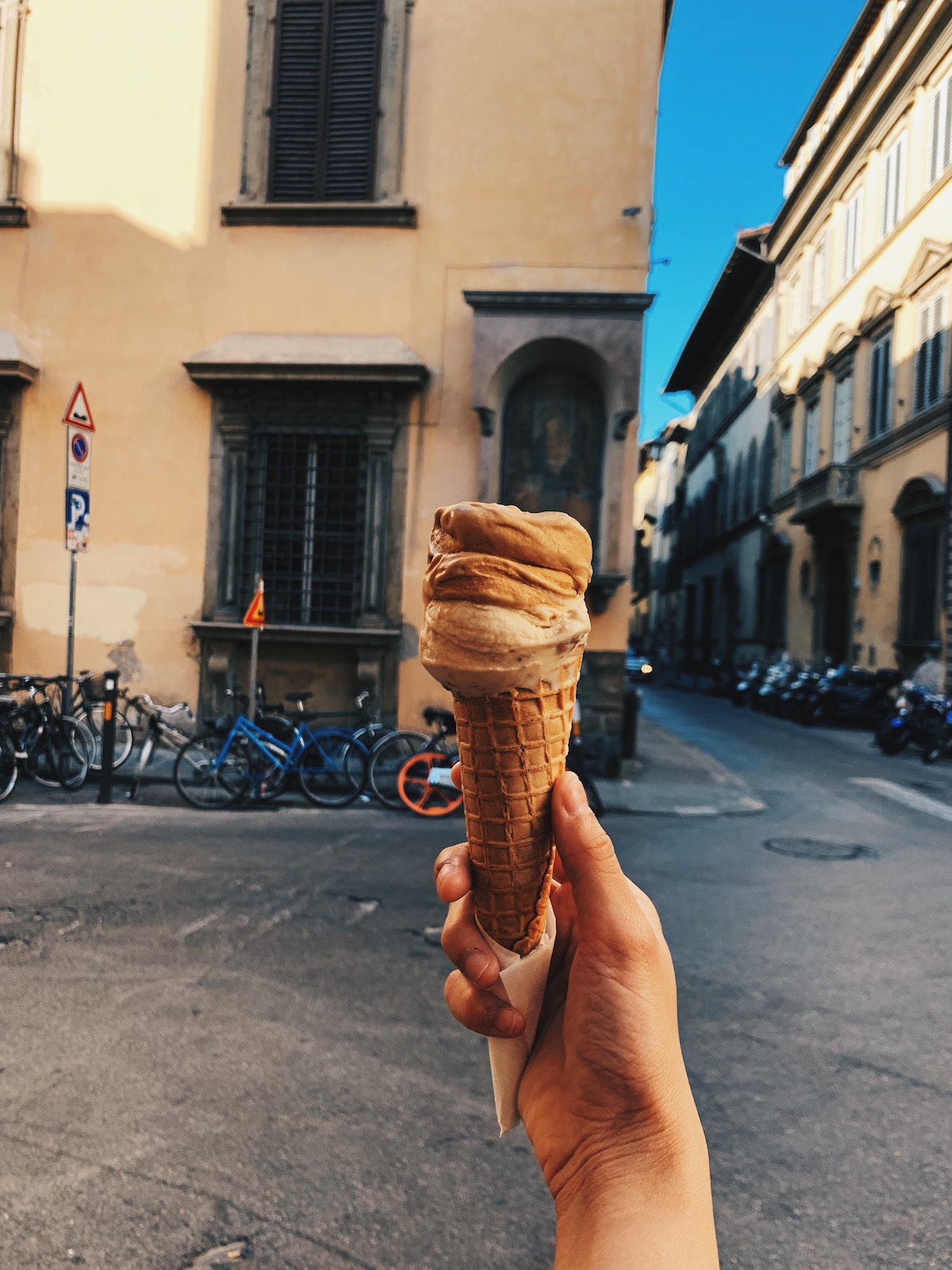 La mano de una persona sosteniendo un cono de helado frente a un edificio