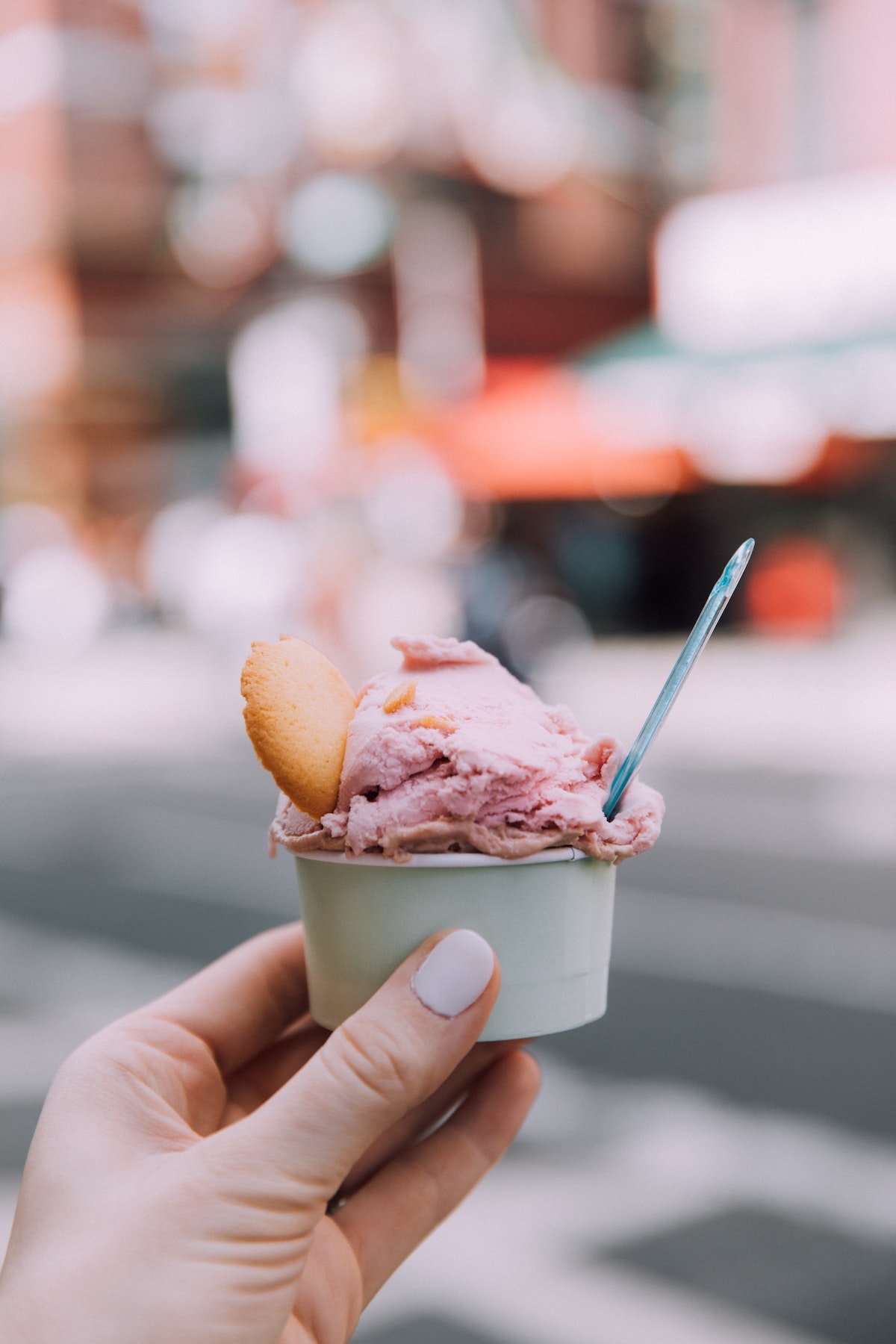 La mano de una persona sosteniendo una pequeña taza de helado rosa adornado con una galleta