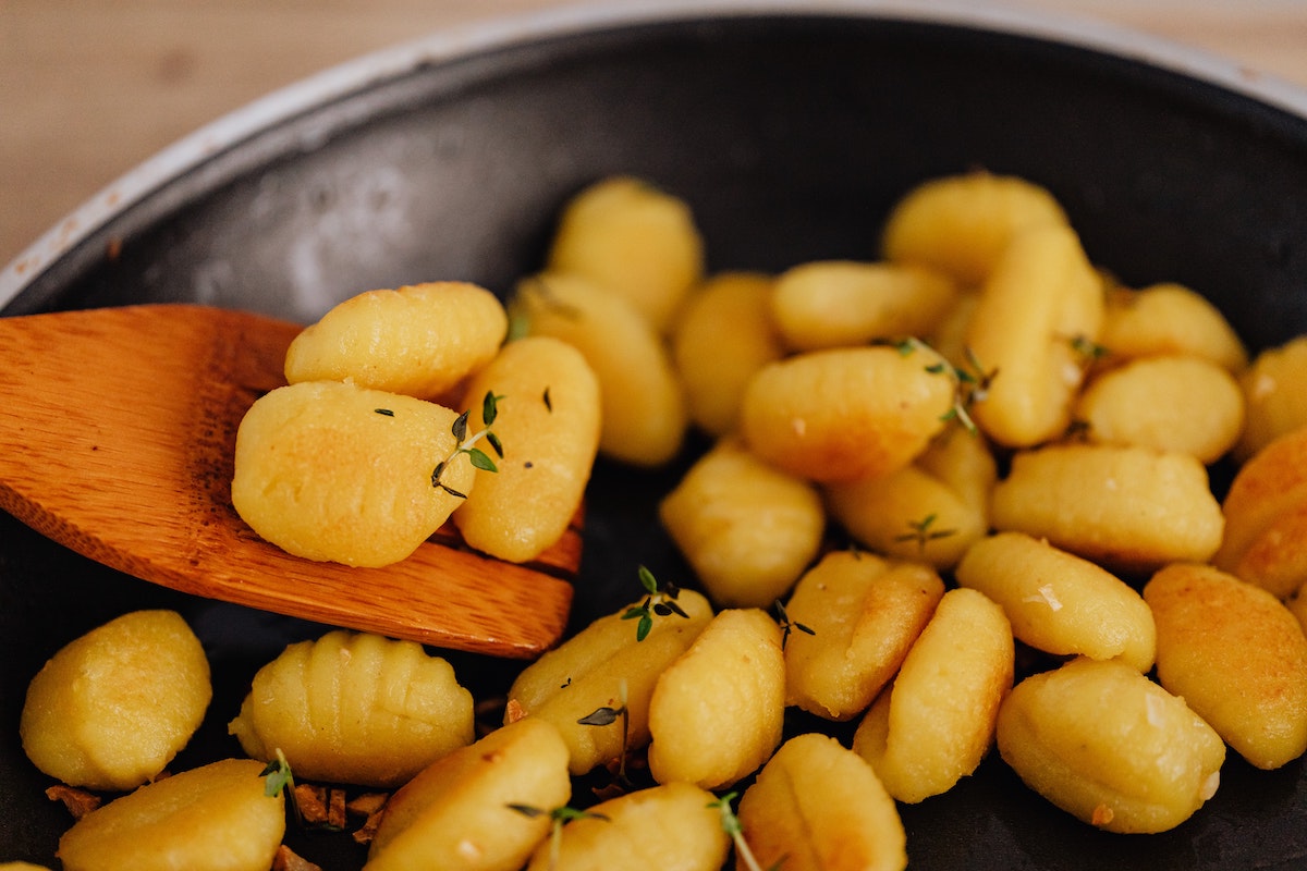 Ñoquis aderezado con hierbas en una sartén con una espátula de madera