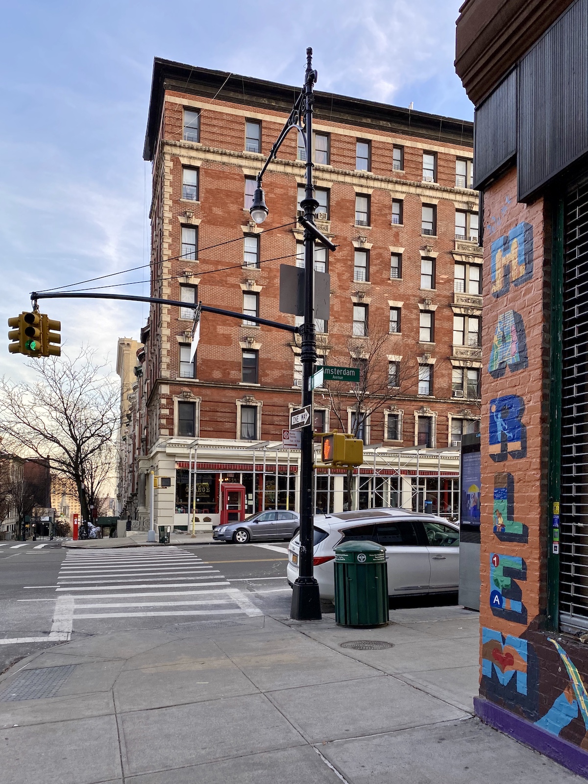 Una intersección en un área urbana con un edificio de ladrillo de varios pisos en el fondo y la palabra "Harlem" pintada en el edificio en primer plano.