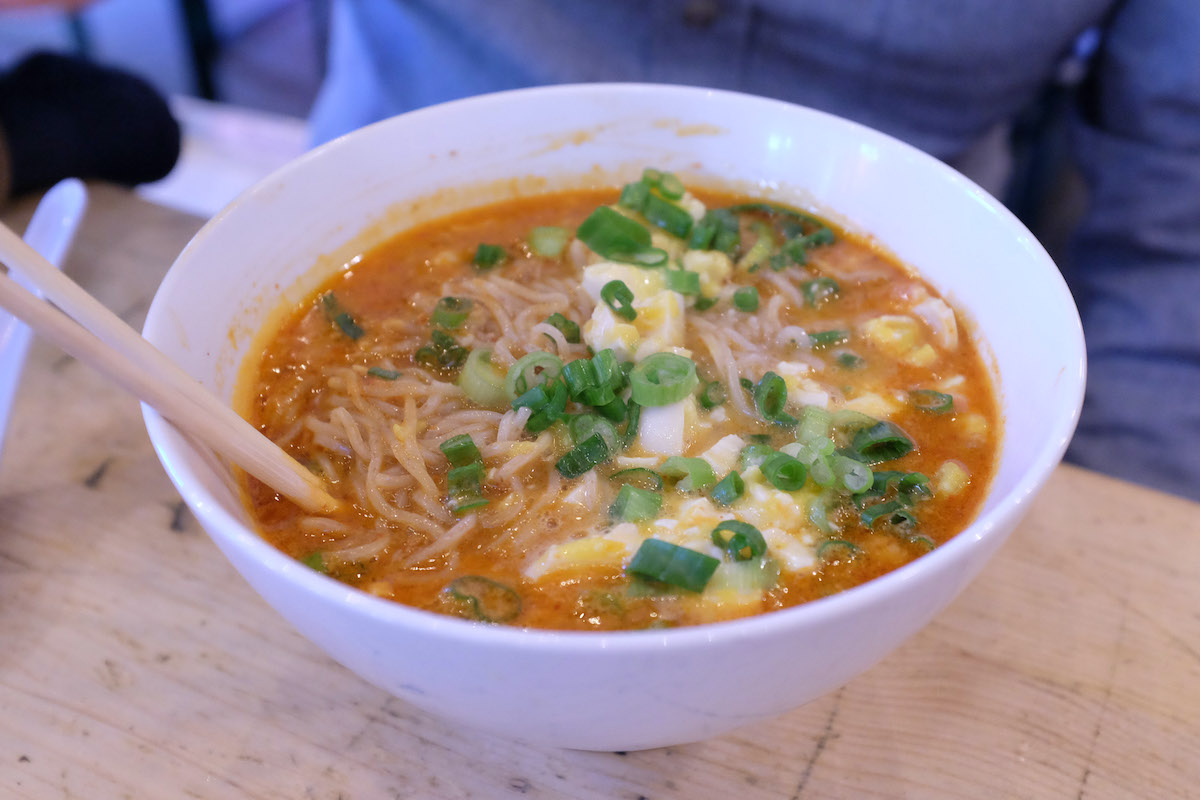 Un tazón de ramen con un caldo rojo cubierto con cebollín