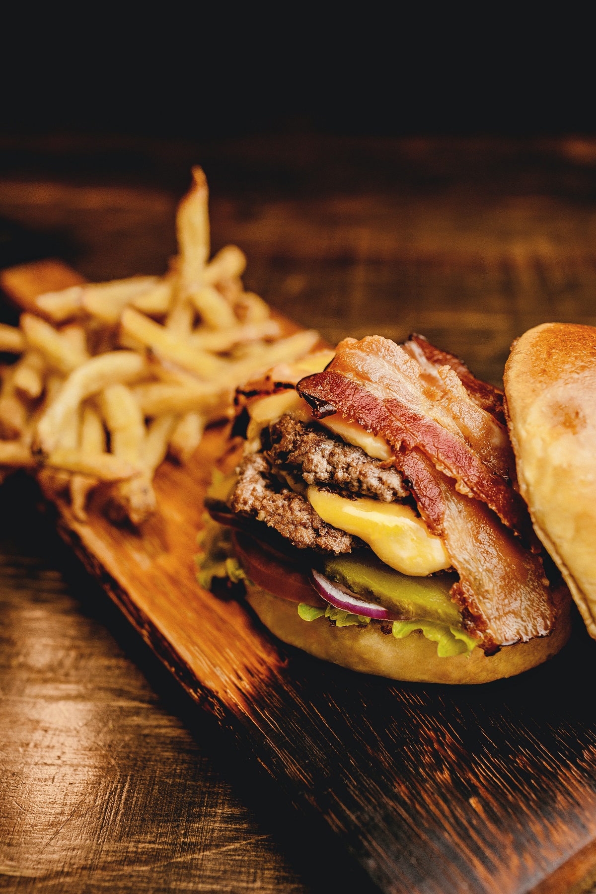 Una hamburguesa con queso con pepinillos y tocino servida en un plato de madera con papas fritas