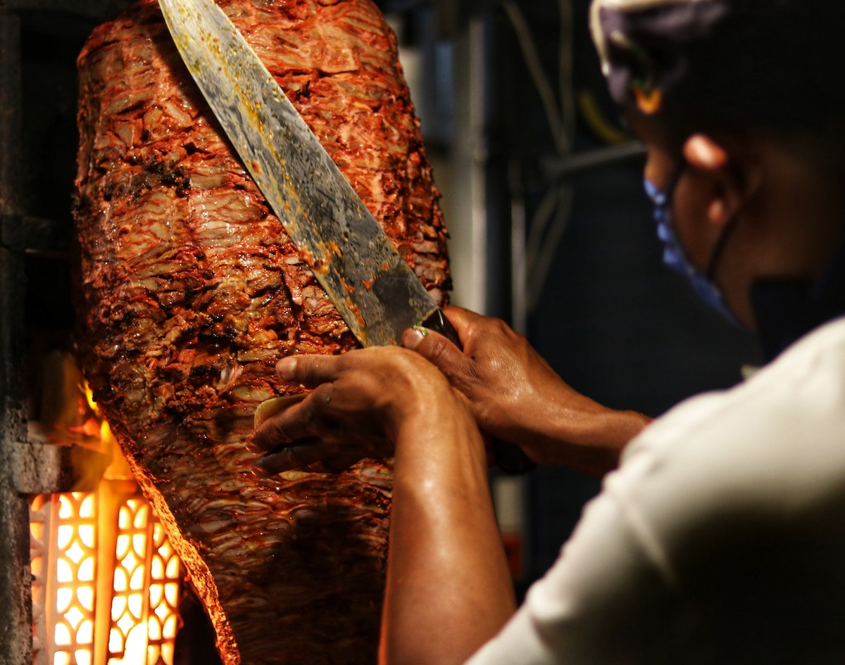 Un hombre que usa un cuchillo grande para cortar carne de kebab de un asador vertical