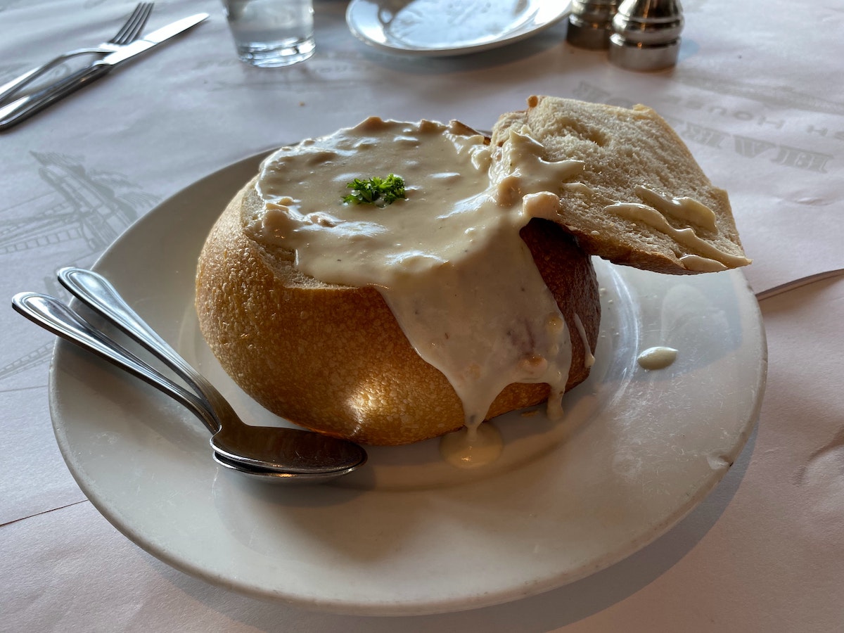Un tazón de pan de masa fermentada relleno con sopa de almejas blancas en un plato blanco. Un plato clásico para probar en San Francisco Pier 39.