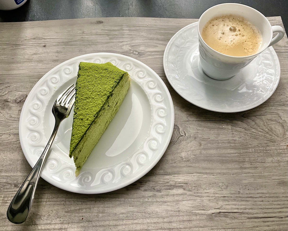Una rebanada de pastel verde en un plato blanco junto a una taza de café en una mesa de madera