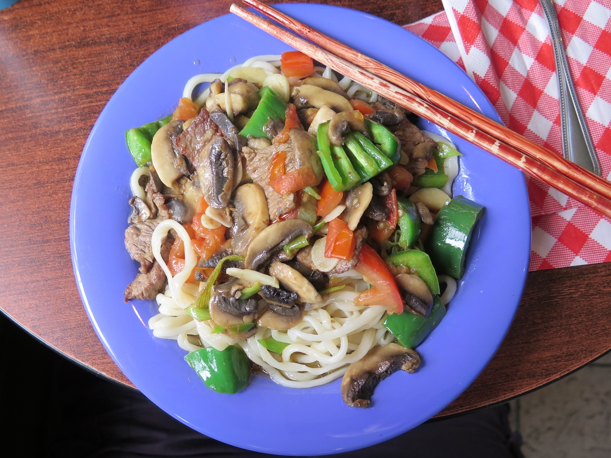 Fotografía cenital de un plato de fideos asiáticos con champiñones y pimientos en un plato azul con un par de palillos rojos claros