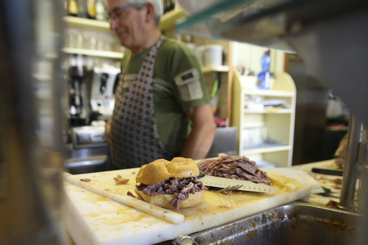 Un sándwich de callos en un mostrador de delicatessen con un hombre con un delantal en el fondo