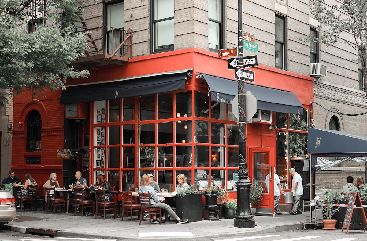 Exterior de un restaurante en la esquina de una calle de la ciudad con paneles rojos alrededor de las ventanas y alas negras