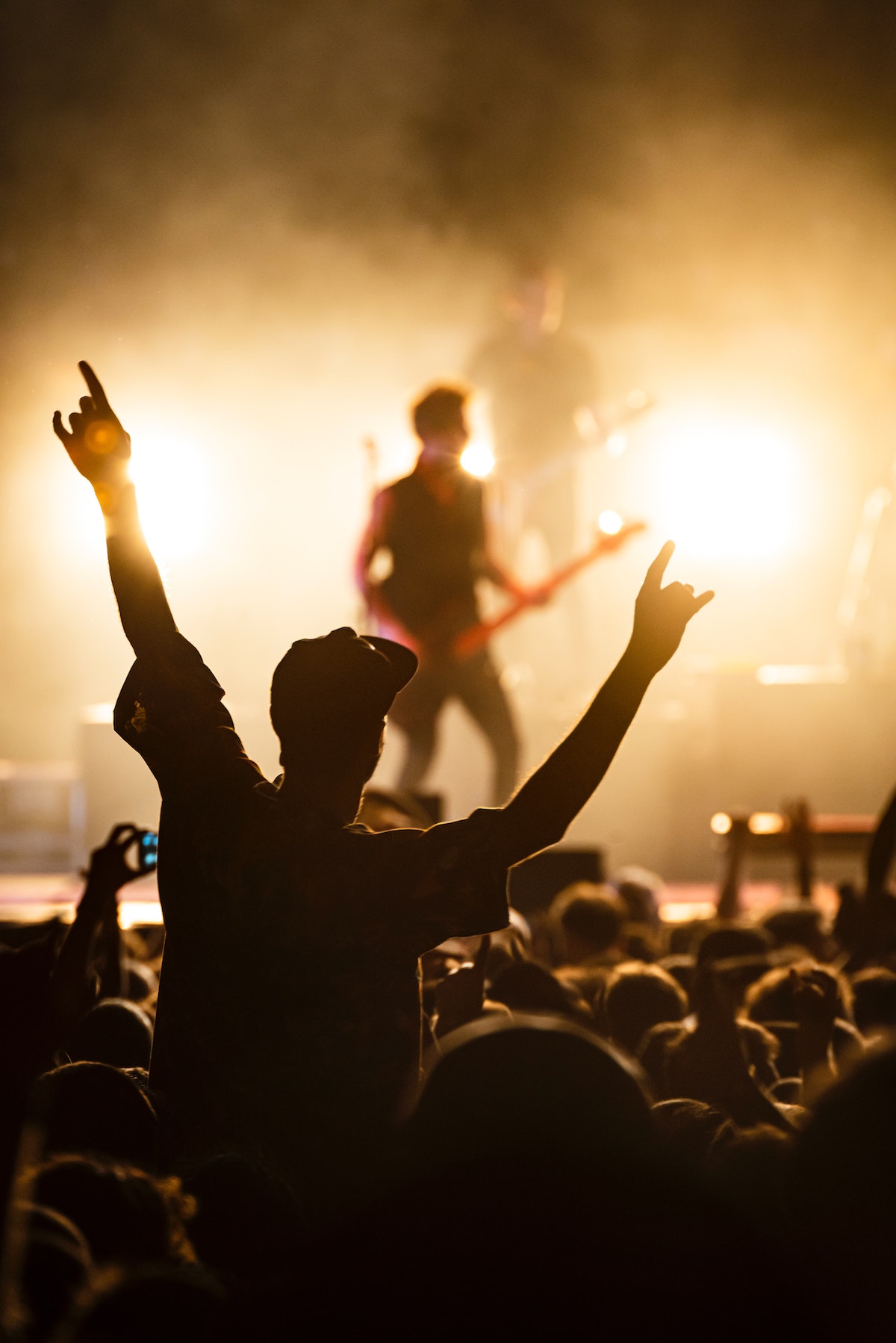 Una persona de pie con ambas manos viendo un concierto de rock en un lugar lleno de gente