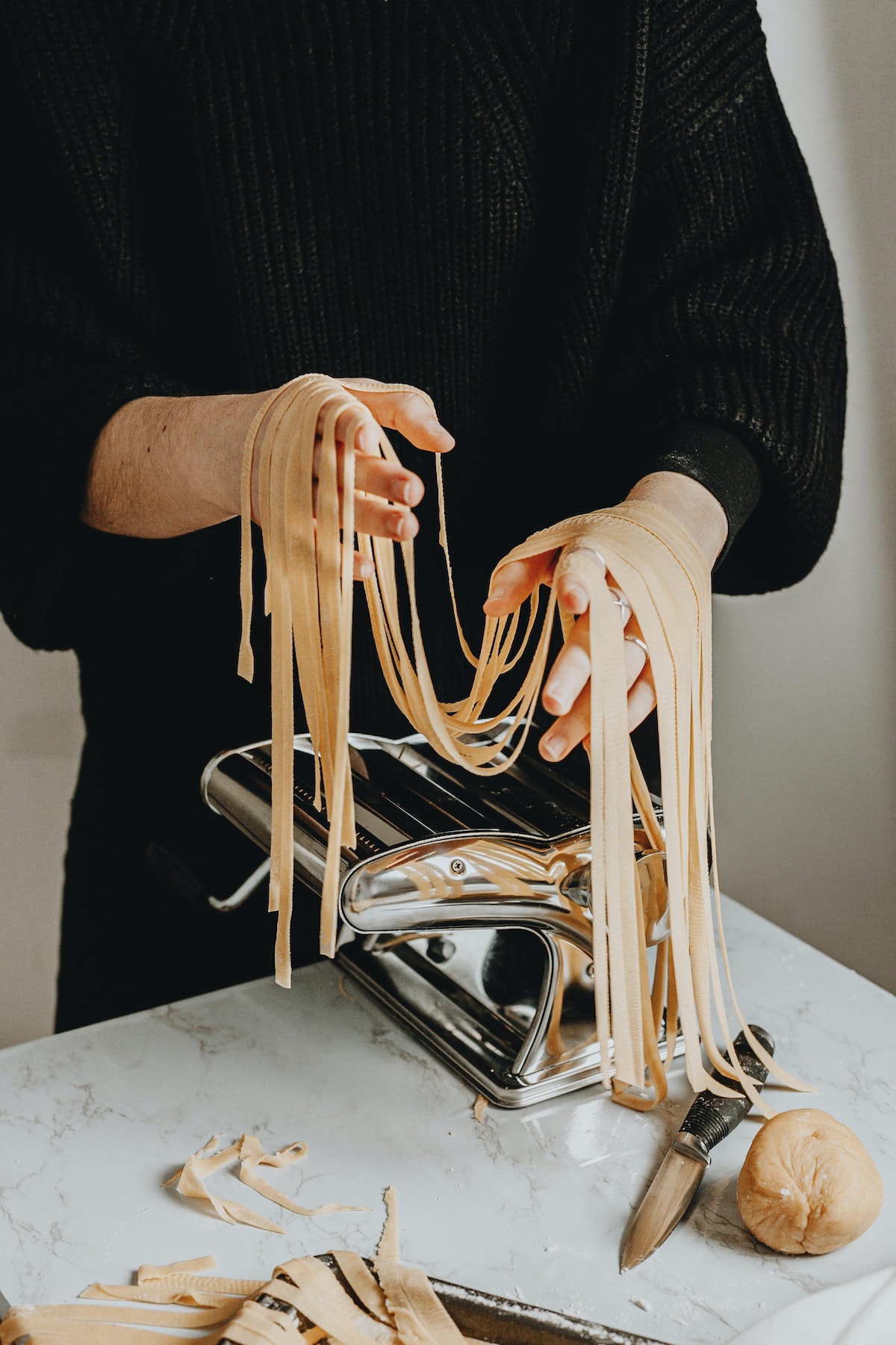 Una persona con una camisa negra con fideos fettuccine frescos.