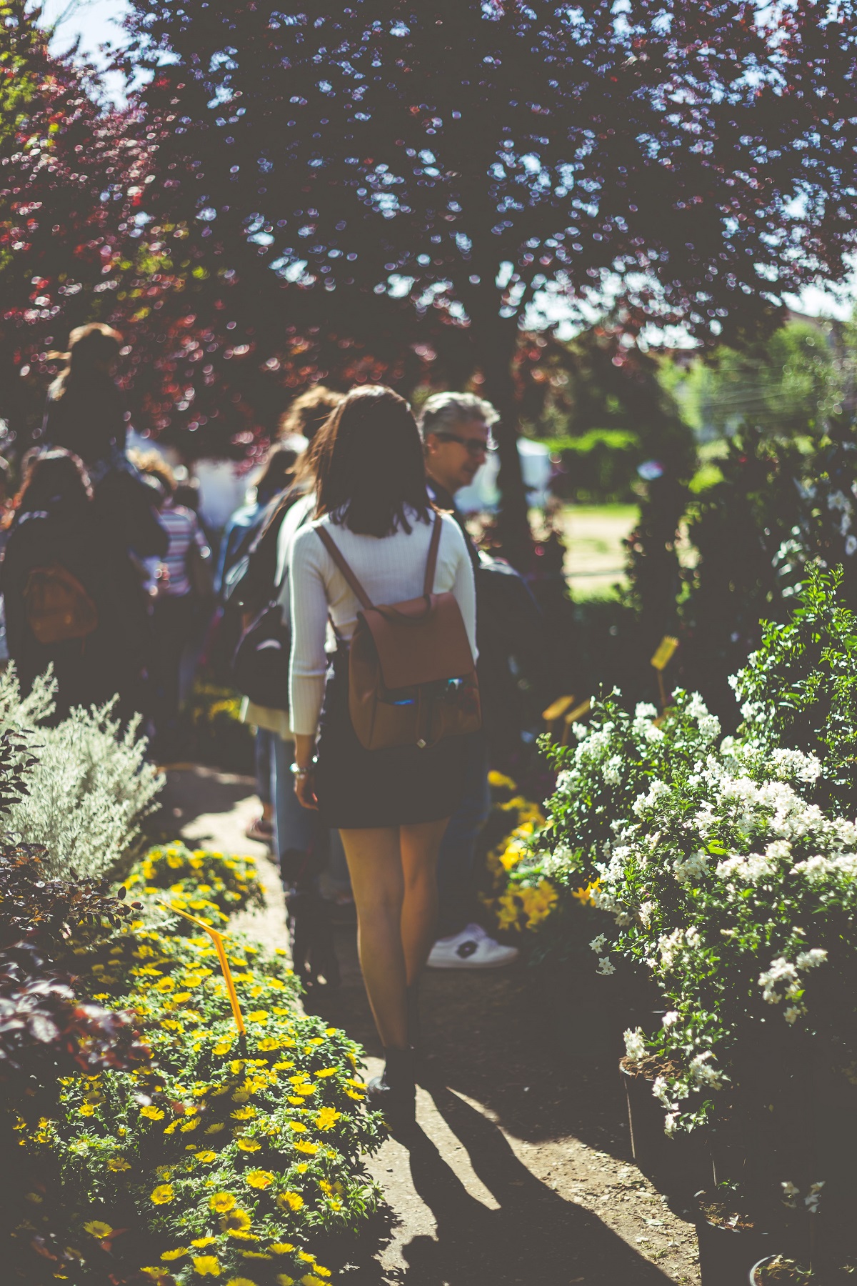 Una mujer joven con una mochila camina por un jardín con flores florecientes