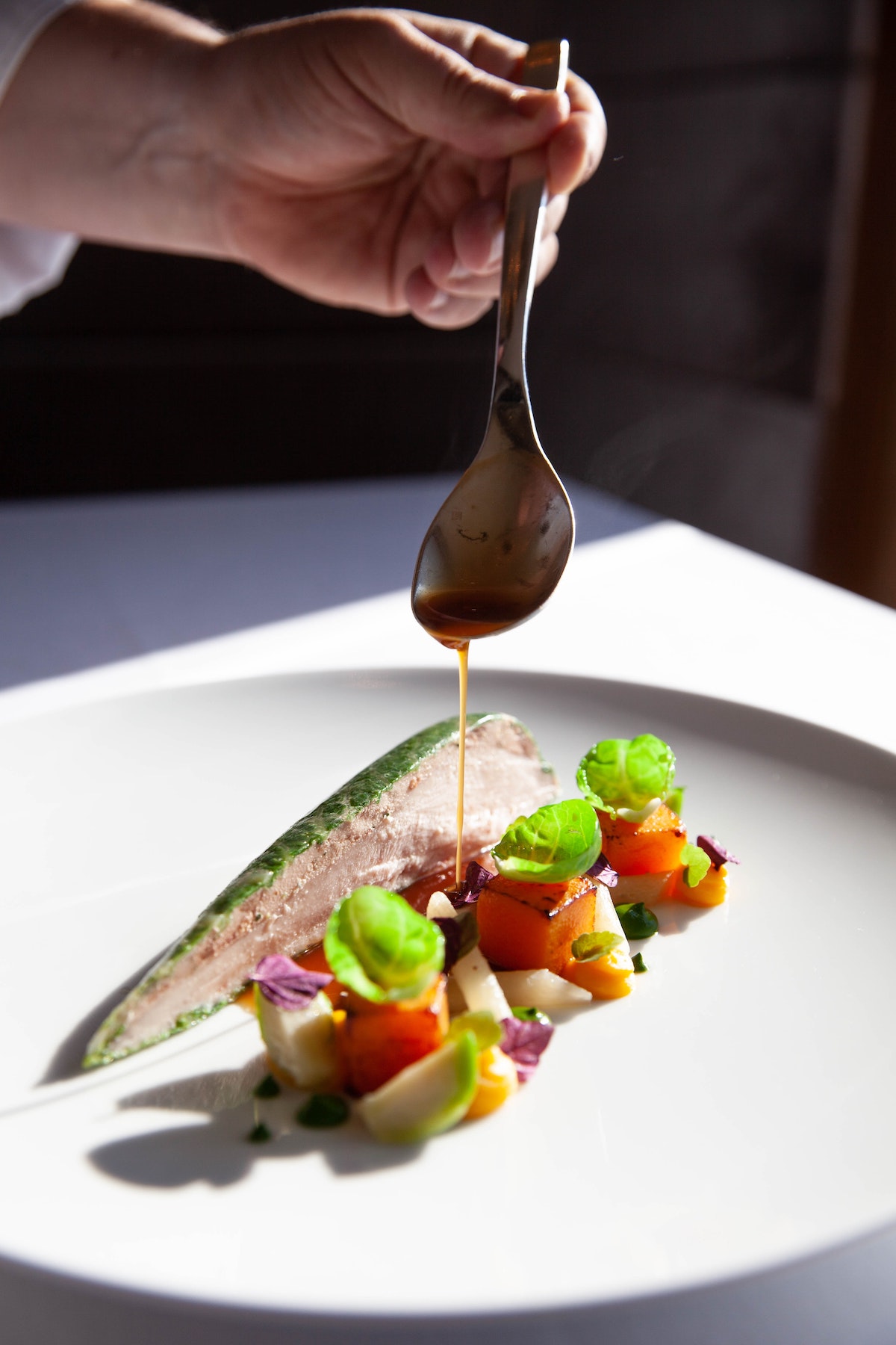 Cucharada de salsa sobre pescado y verduras ingeniosamente presentada en un plato blanco
