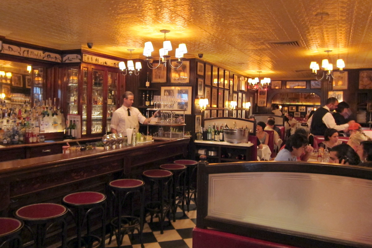Un bar antiguo con baldosas a cuadros, paneles de madera oscura y filas de cuadros enmarcados en la pared.