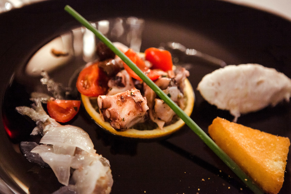 Una presentación moderna de un plato de pulpo y verduras servido en un plato negro