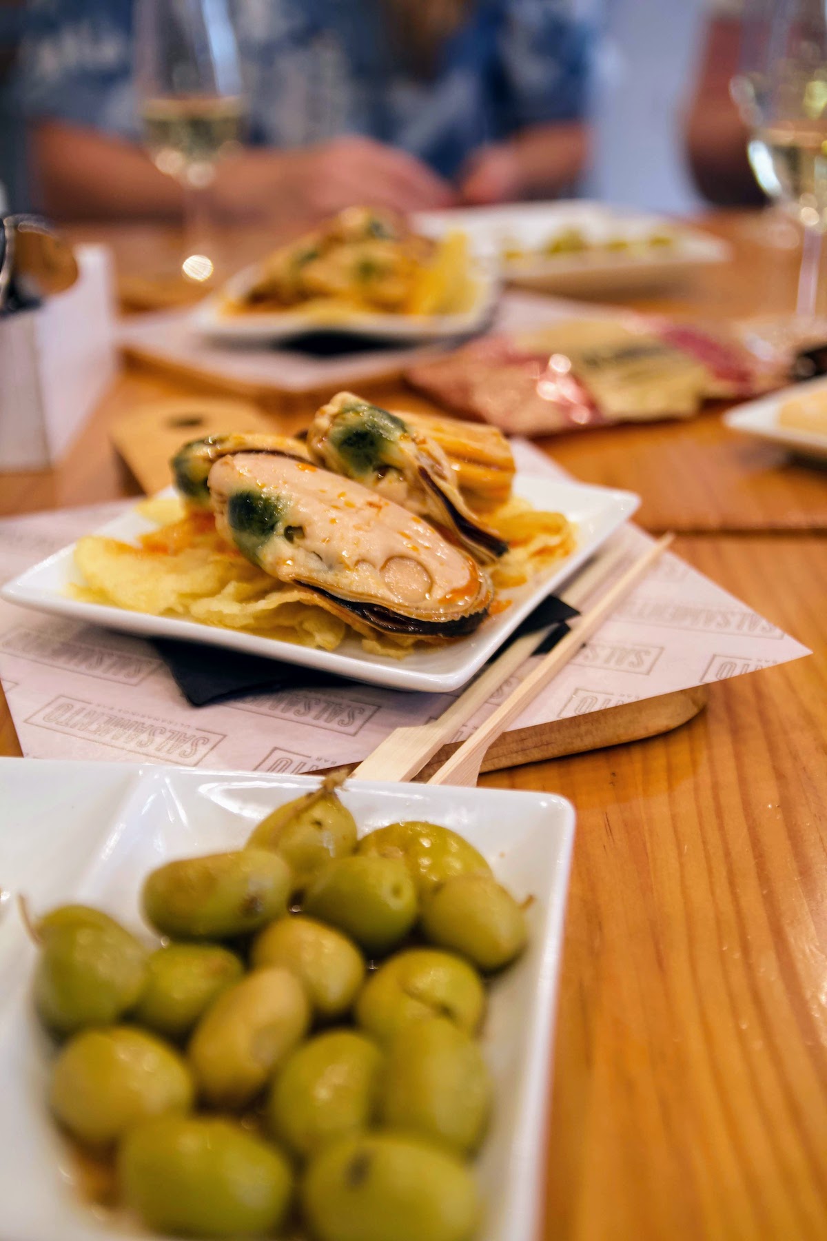 Pequeños platos de mejillones y aceitunas verdes sobre una mesa de madera