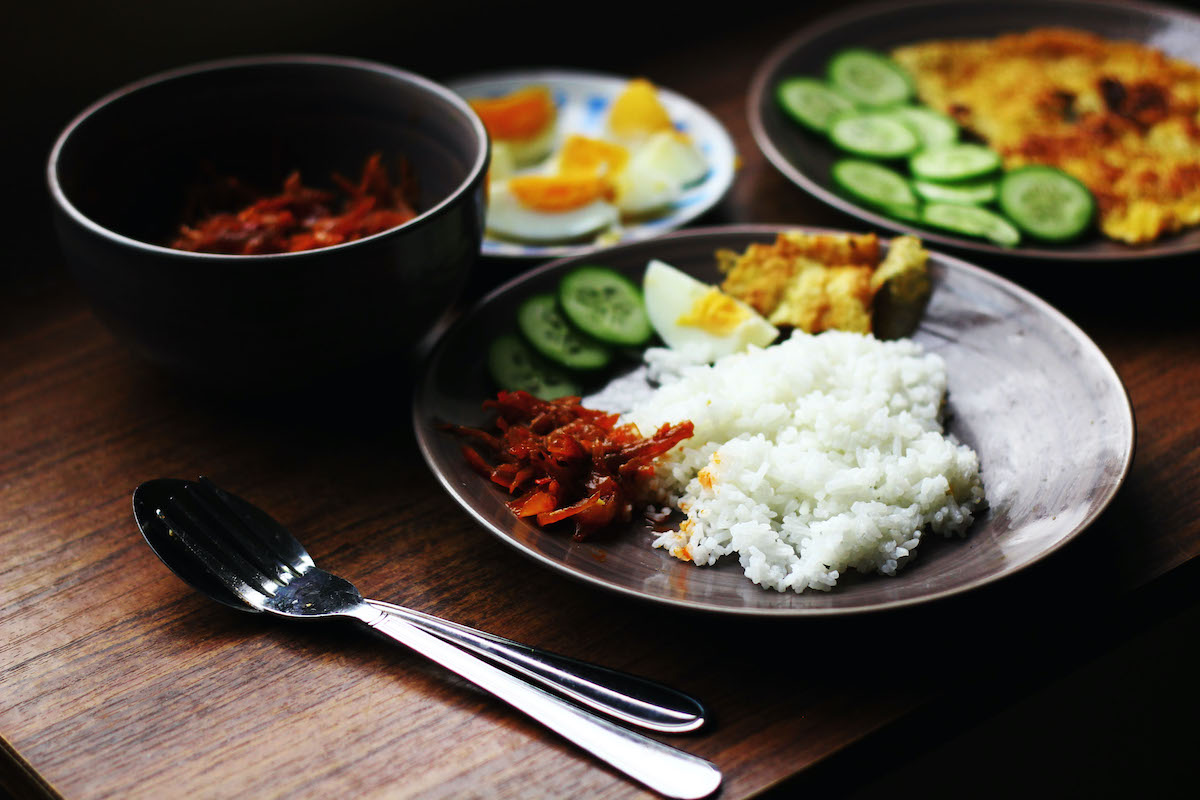 Algunos platos de Malasia en una mesa con un plato de arroz blanco y verduras en primer plano.