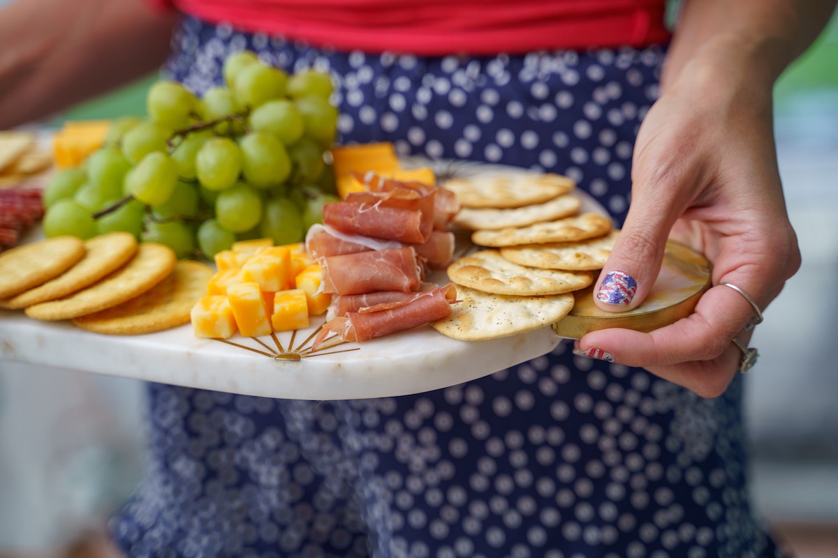 uno con un plato blanco cubierto con queso, fiambres, galletas saladas y fruta