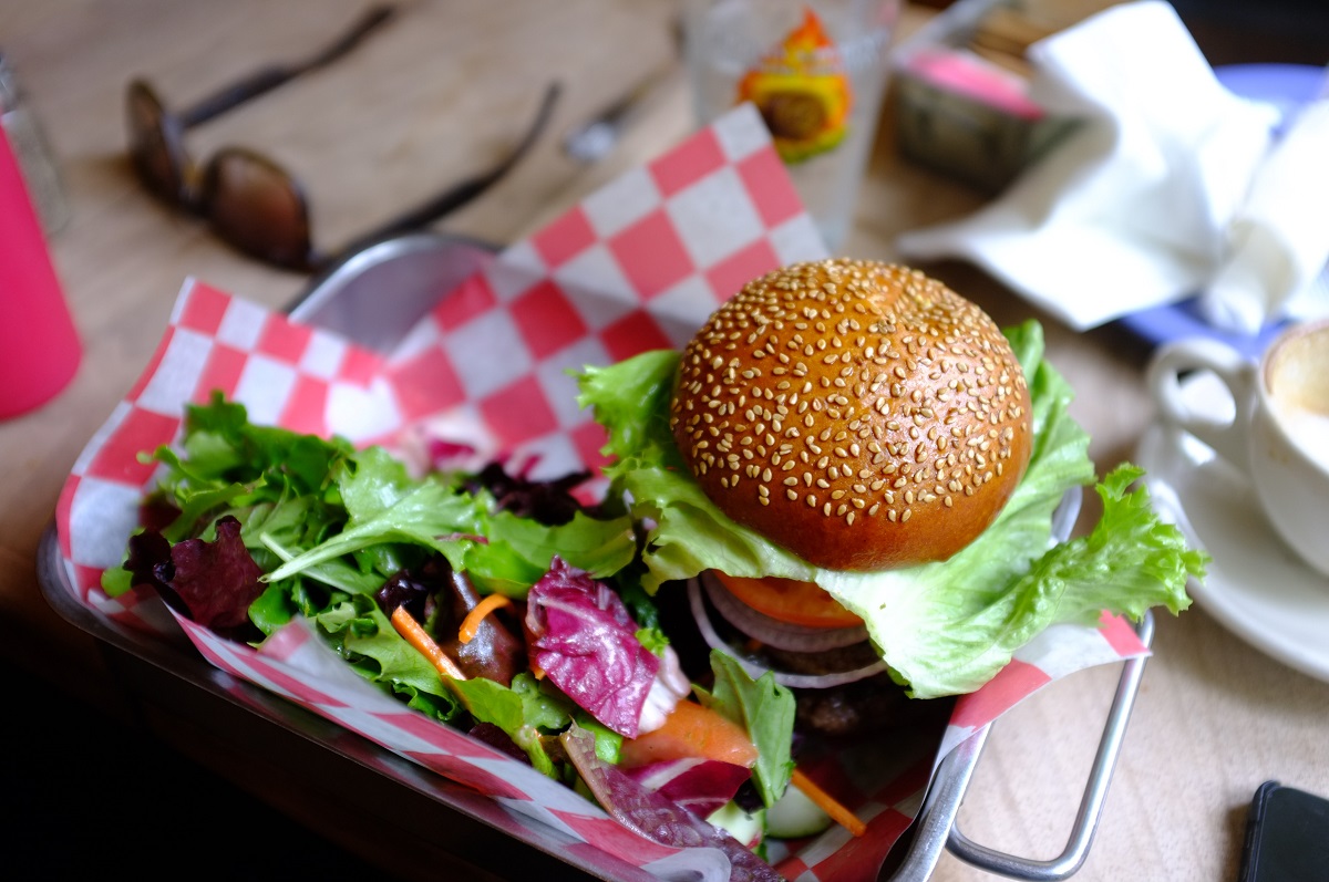 Una hamburguesa tradicional en un bollo de semillas de sésamo con ensalada servida en una bandeja de metal con servilletas a cuadros rojos y blancos
