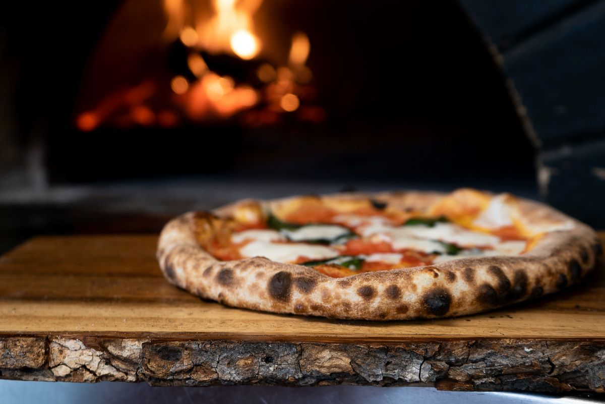 pizza en un estante de madera con un fuego de piedra encima