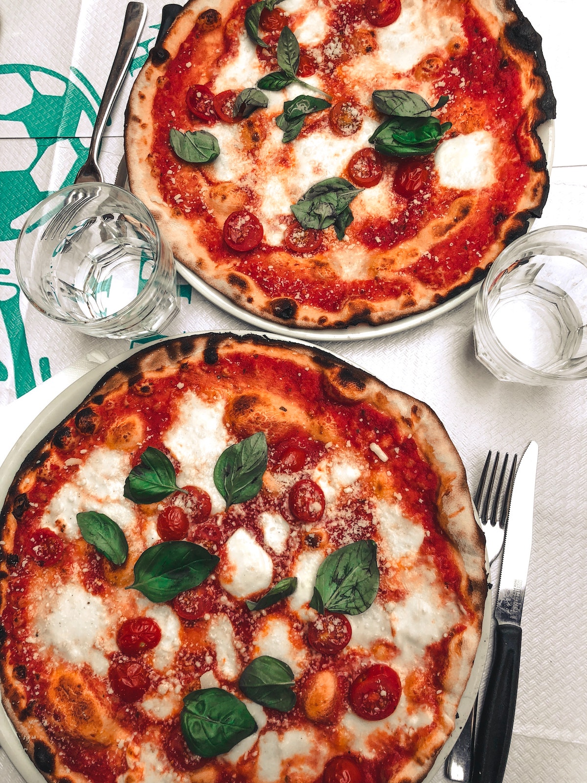Una fotografía cenital de dos pizzas margherita enteras con tomate, queso, albahaca y mozzarella