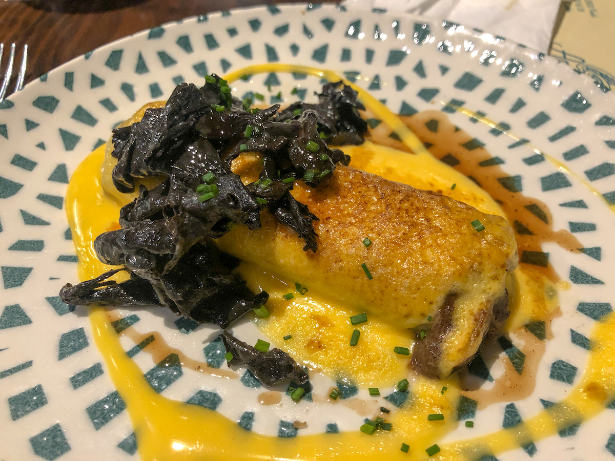Canelones de rabo de toro servidos con verduras de hoja verde cocidas y salsa amarilla.