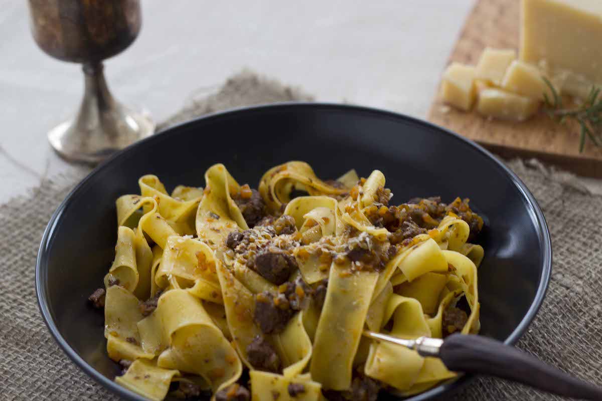 Fideos anchos de pasta con ragú de jabalí en un plato negro