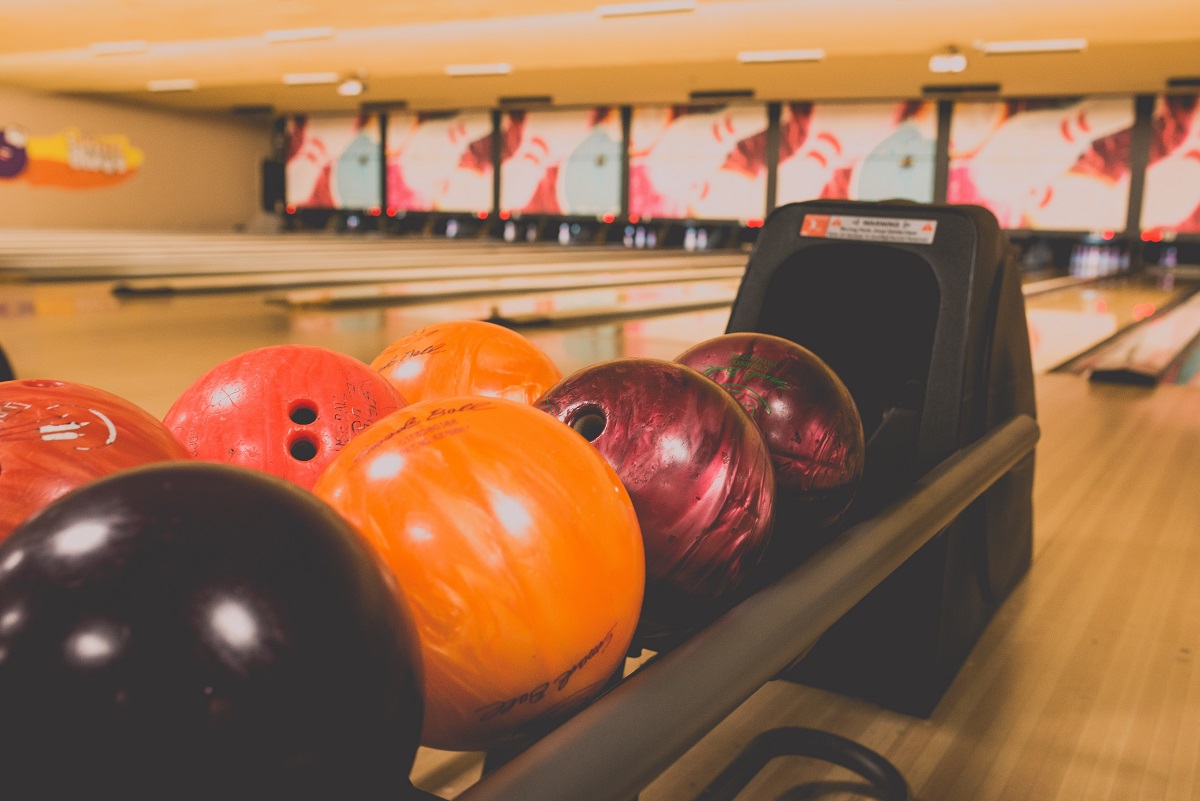 Bolas de bolos naranjas y moradas alineadas en un estante frente a las pistas de bolos