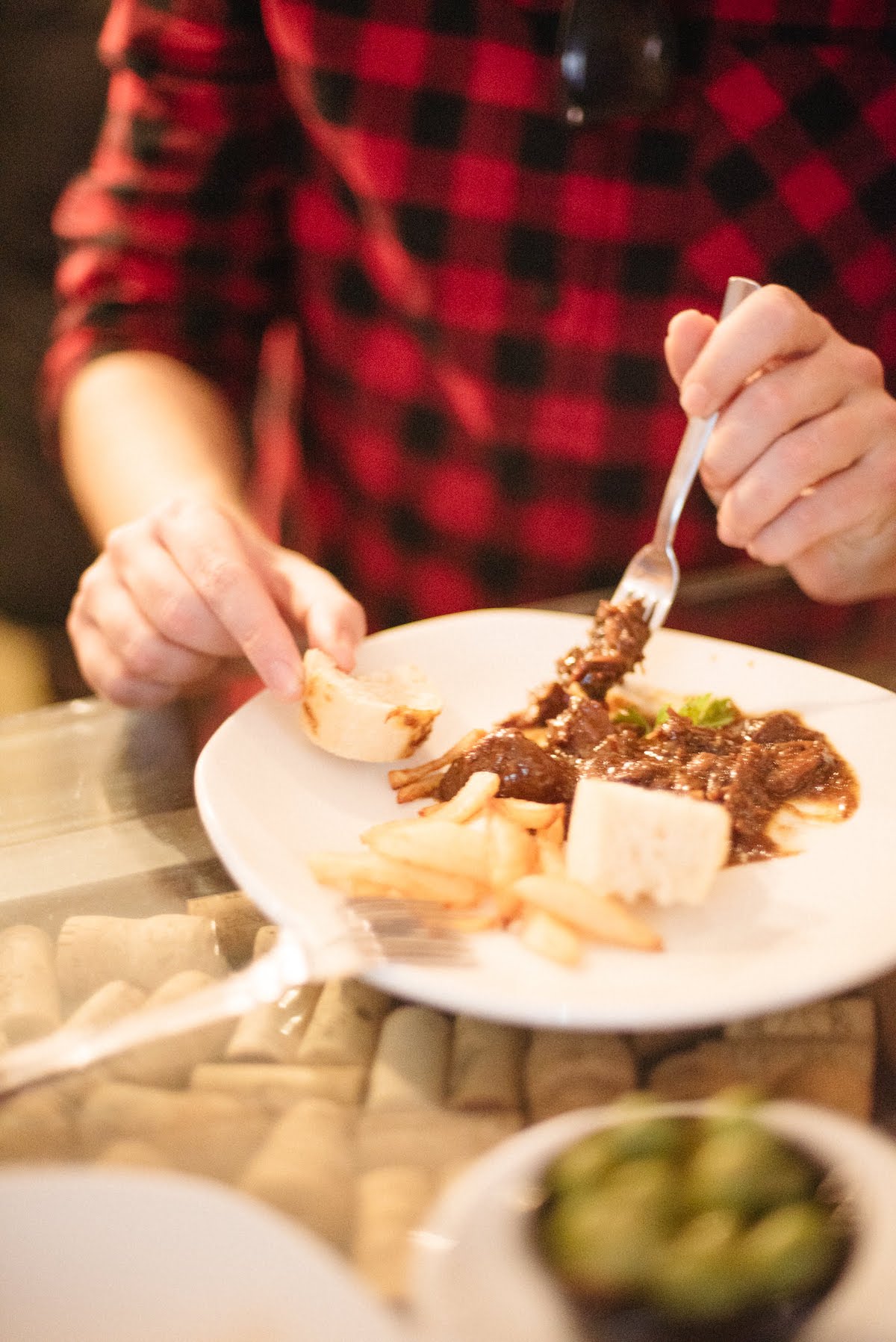Una persona con una camisa a cuadros roja y negra comiendo un plato de carne con un pequeño trozo de pan