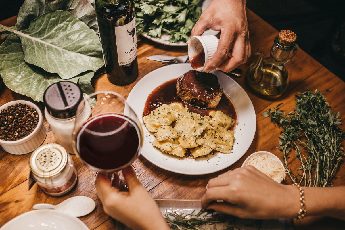una mesa decorada con pasta y un plato de carne y una copa de vino tinto