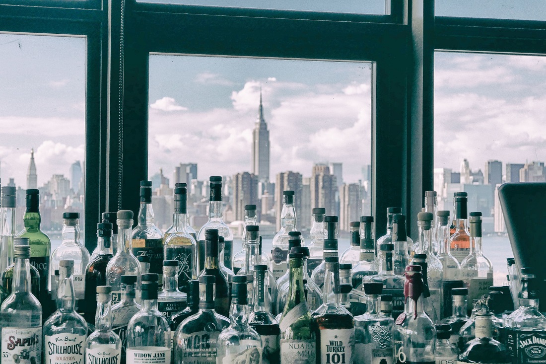 Un mostrador lleno de botellas de licores frente a una ventana con vista al horizonte de Manhattan