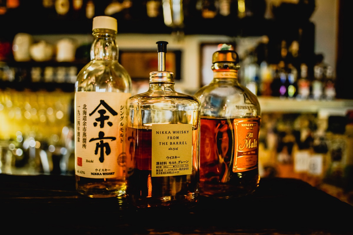 3 elegantes botellas de whisky alineadas en un mostrador y una barra al fondo