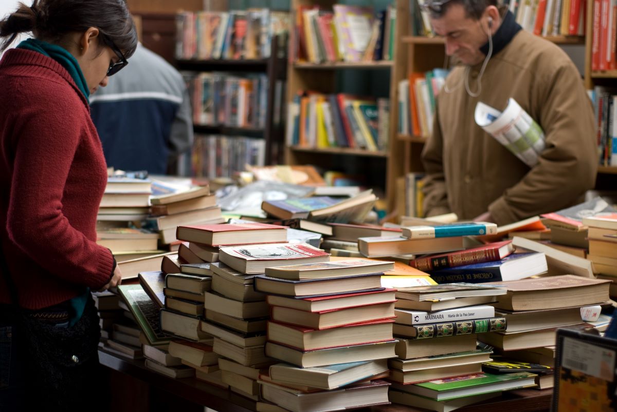 mujer-y-hombre-de-pie-cerca-de-montones-de-libros-en-una-librería