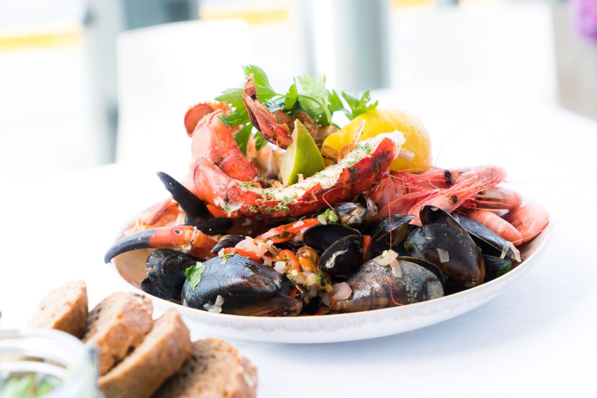 un plato blanco de mejillones y cangrejo sobre un mantel blanco y pan 
