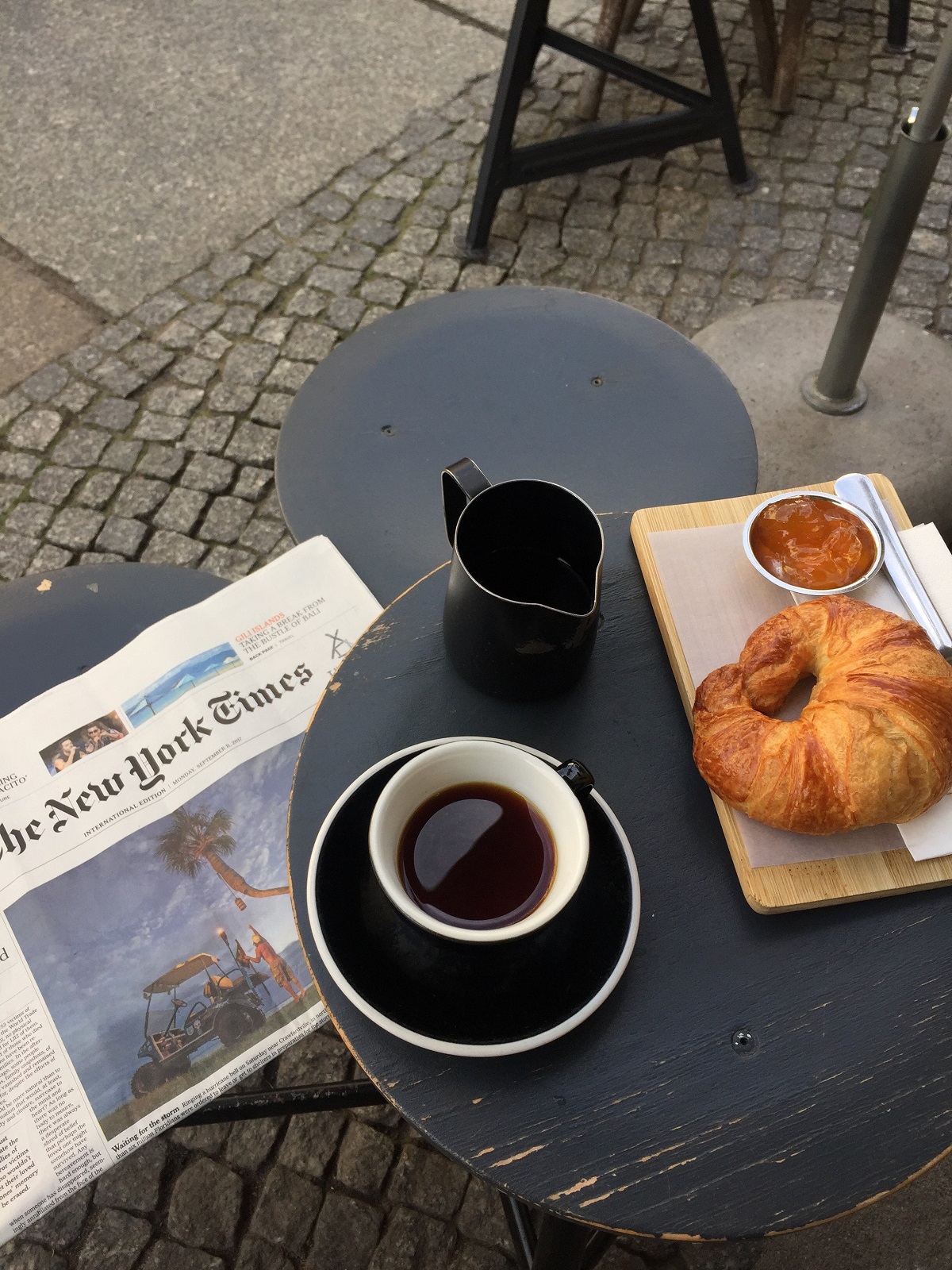Croissant y café solo en una mesa al aire libre con el periódico New York Times