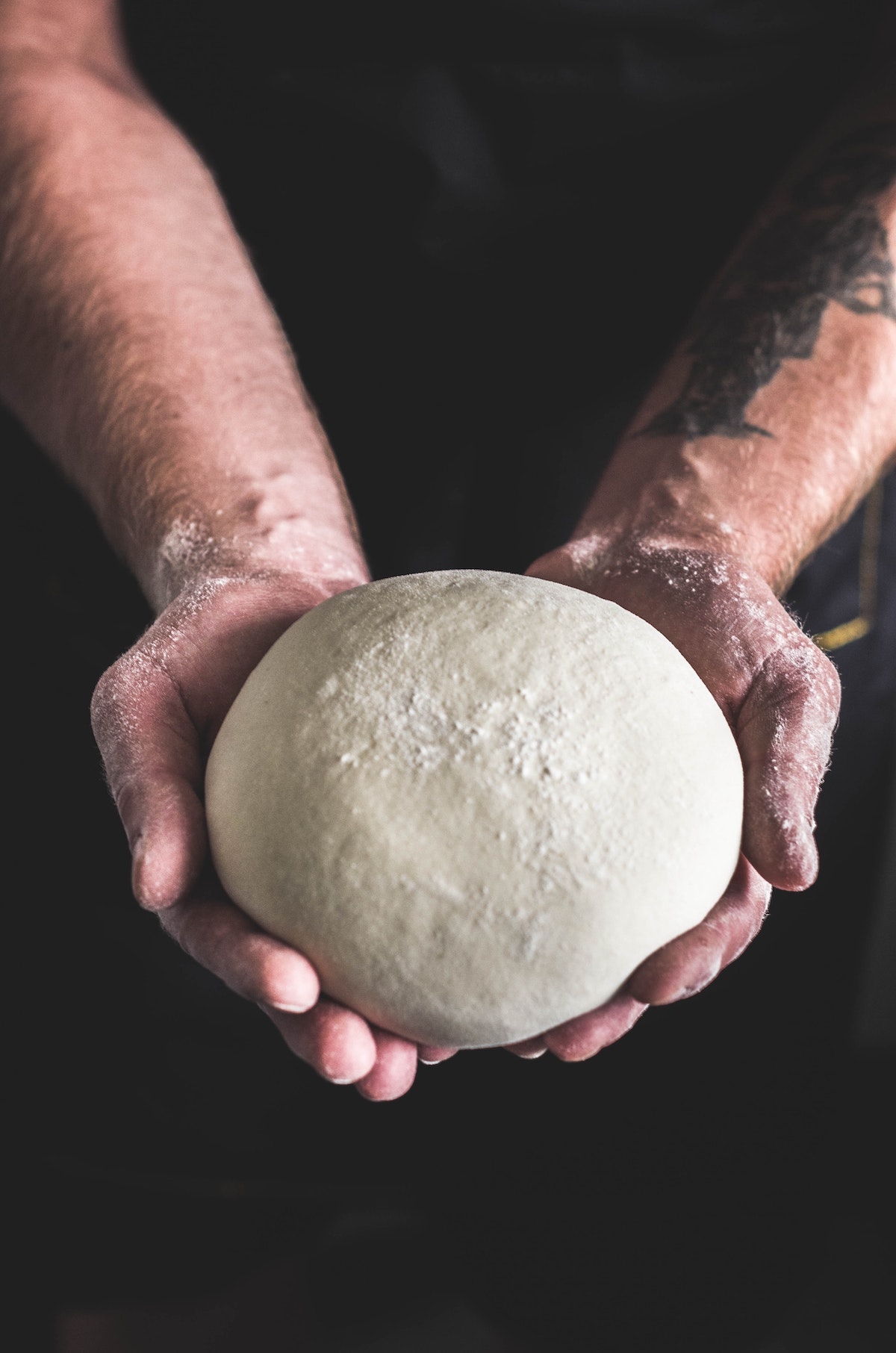 Manos de una persona que sostiene una bola de masa para pizza.