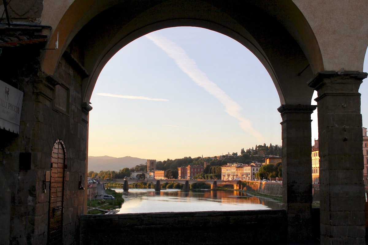 Una vista de una ciudad a lo largo de la orilla del río construida a través de un arco y un puente visible en el fondo
