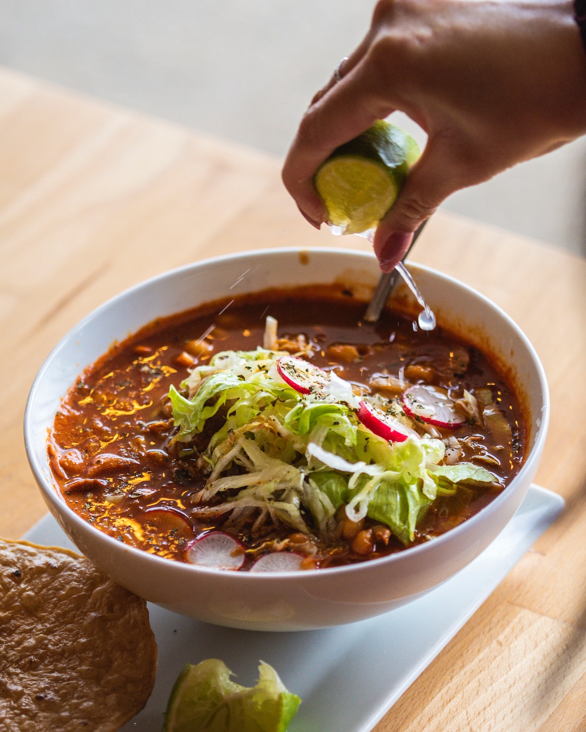 La mano de una persona exprimiendo limón sobre un tazón de sopa de pozole mexicano