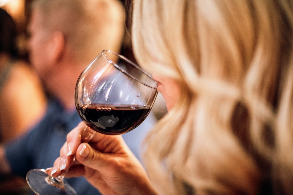 Mujer rubia que huele una copa de vino tinto