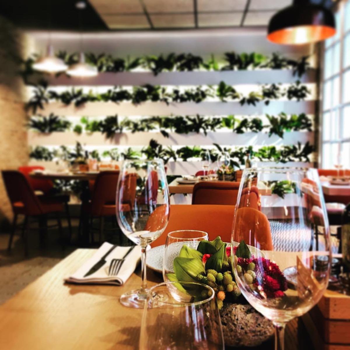 Al fondo se puede ver una mesa puesta con dos copas de vino vacías y una pared cubierta de hiedra.