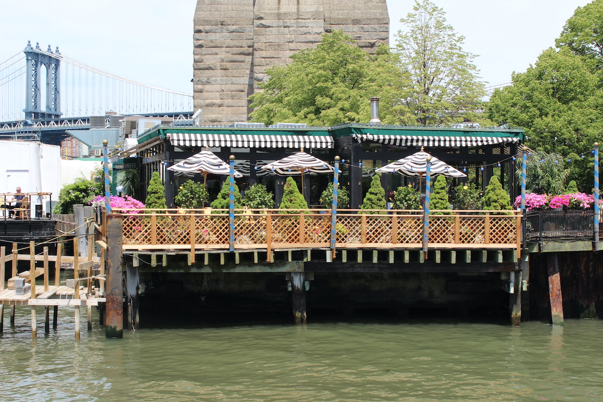 Un pequeño restaurante romántico en Nueva York con flores y sombrillas en el patio encaramado en un muelle sobre un cuerpo de agua