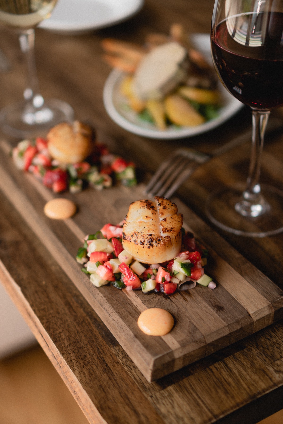 Presentación moderna de comida en una tabla de madera junto a dos copas de vino en un restaurante romántico en Nueva York