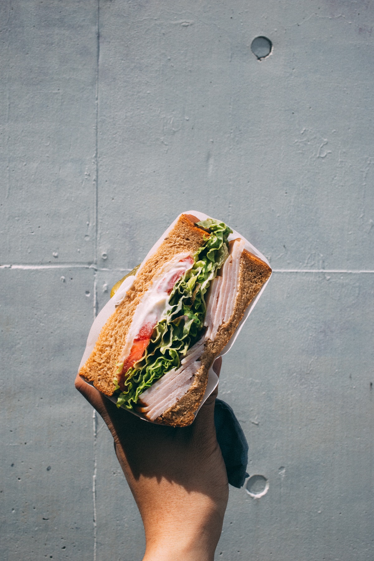 La mano de una persona con un sándwich relleno de carne y verduras de hoja verde