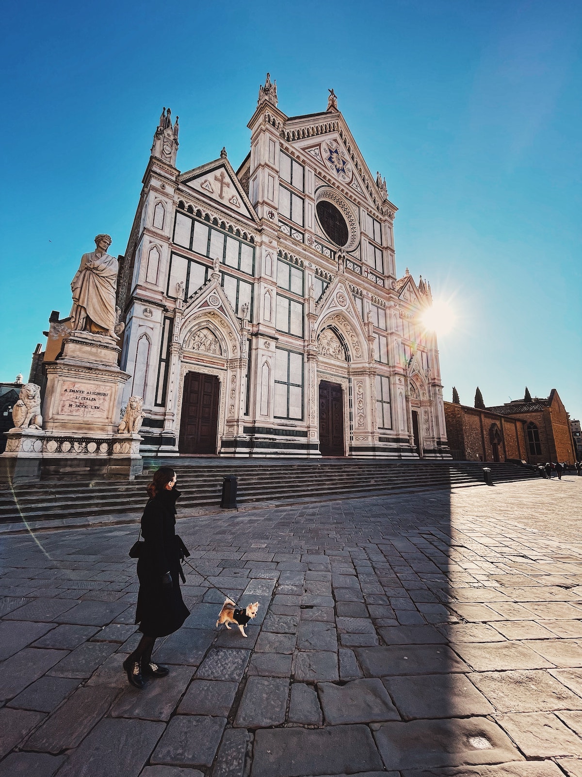 Una mujer paseando a su perro frente a una gran iglesia en Florencia, Italia, en un día despejado.