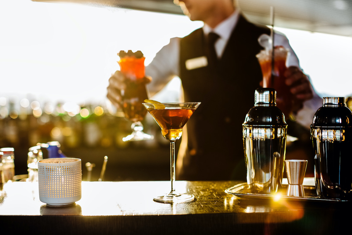 Un cóctel marrón en una copa de martini en una terraza al aire libre con un barman uniformado al fondo