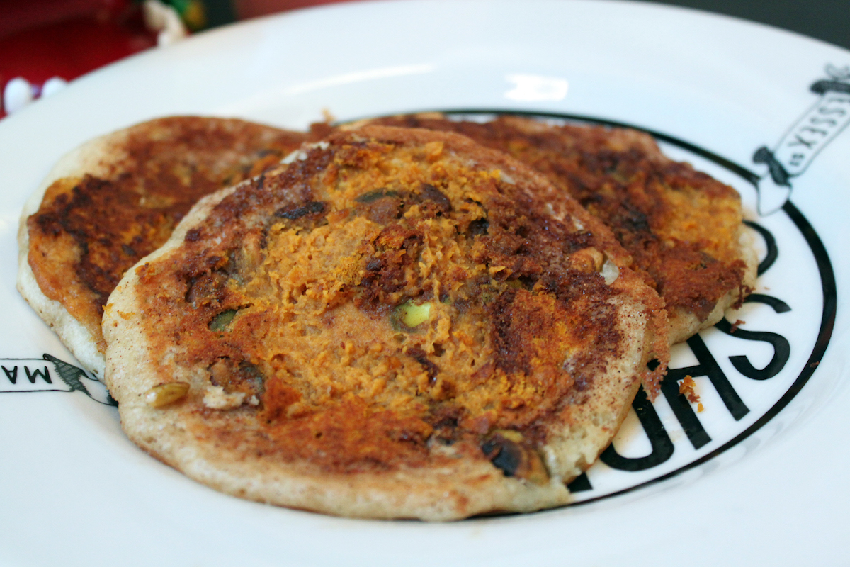 Tres panqueques con calabaza glaseada, mantequilla de maní y pistachos en un plato blanco