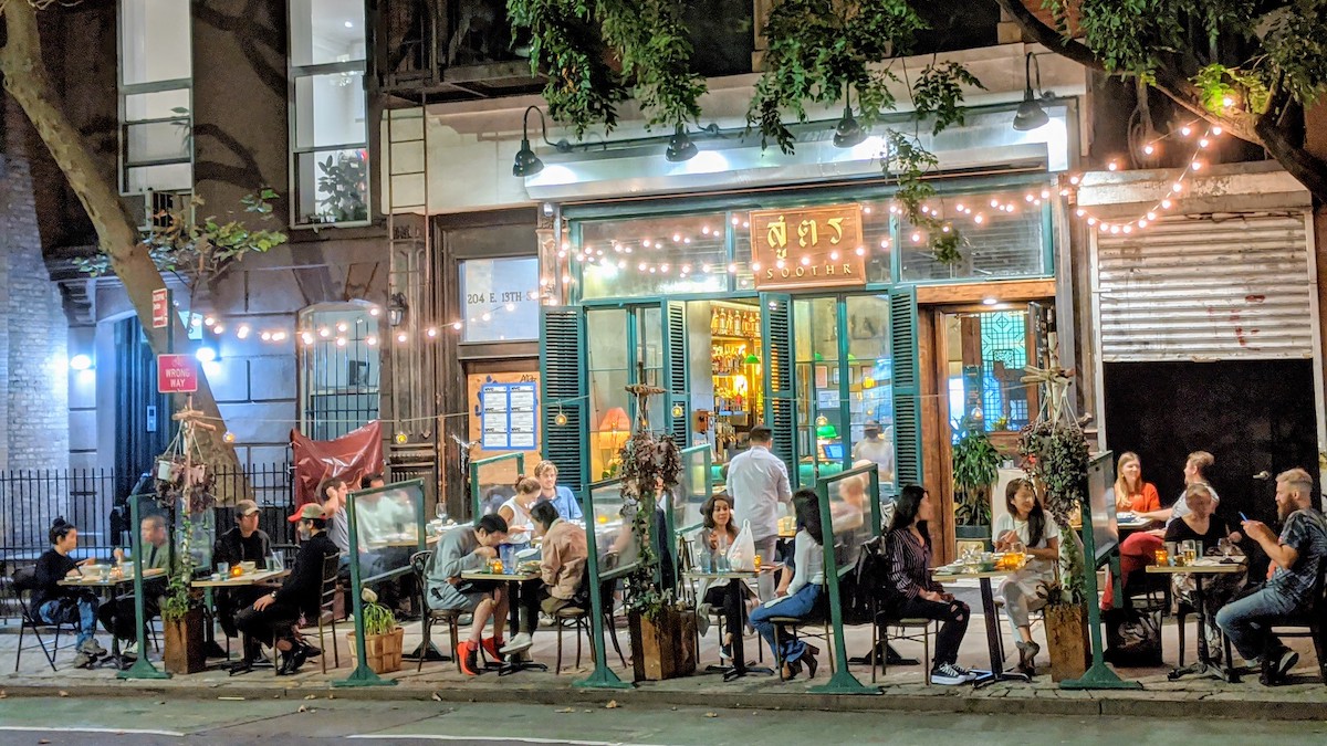 Gente comiendo en la terraza de un restaurante en la acera con luces de cuerda arriba