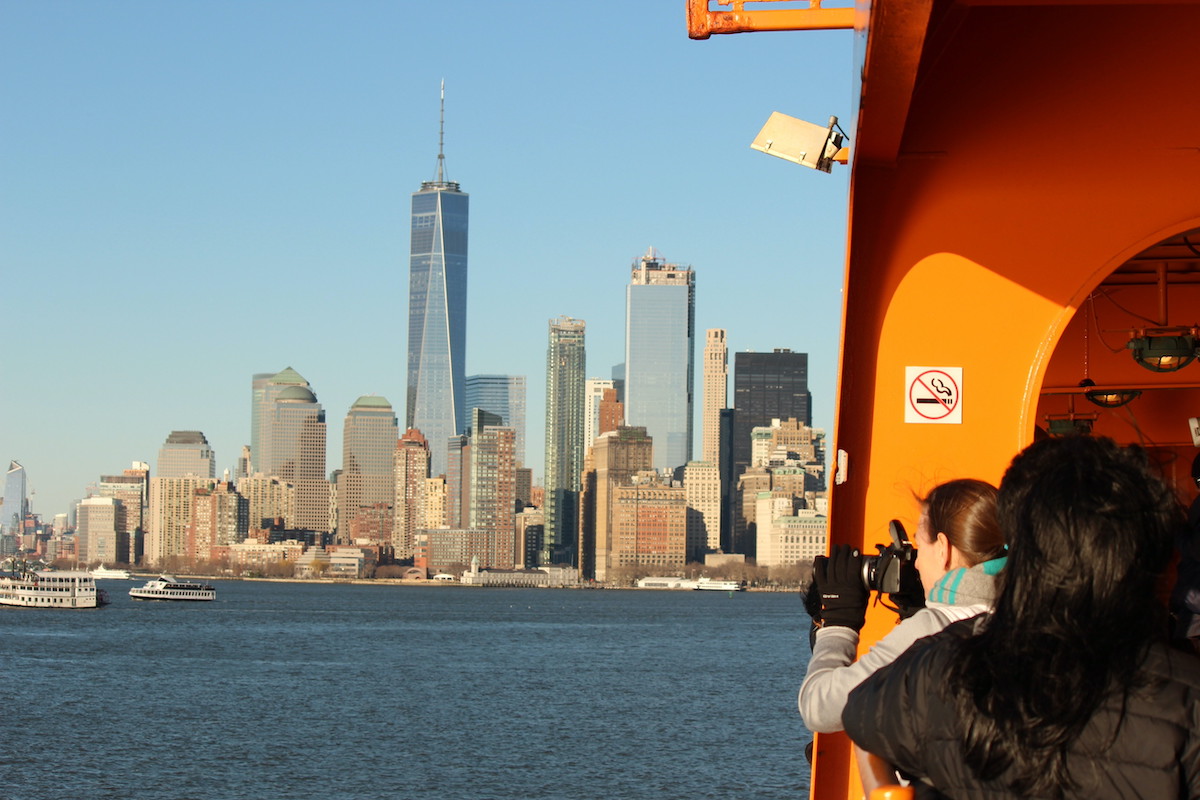 Vista de personas en un ferry naranja tomando fotos del horizonte de Manhattan.