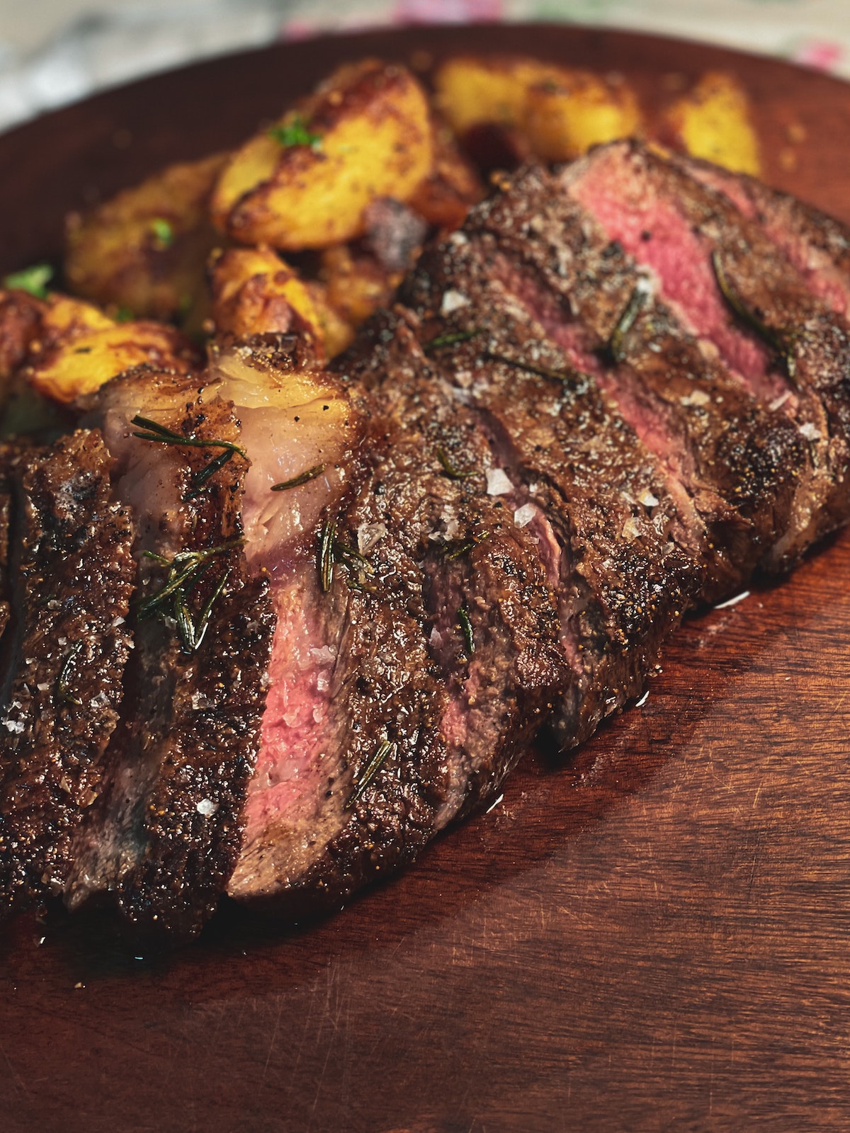 Bistec raro medio en rodajas con gajos de patata en un plato de madera