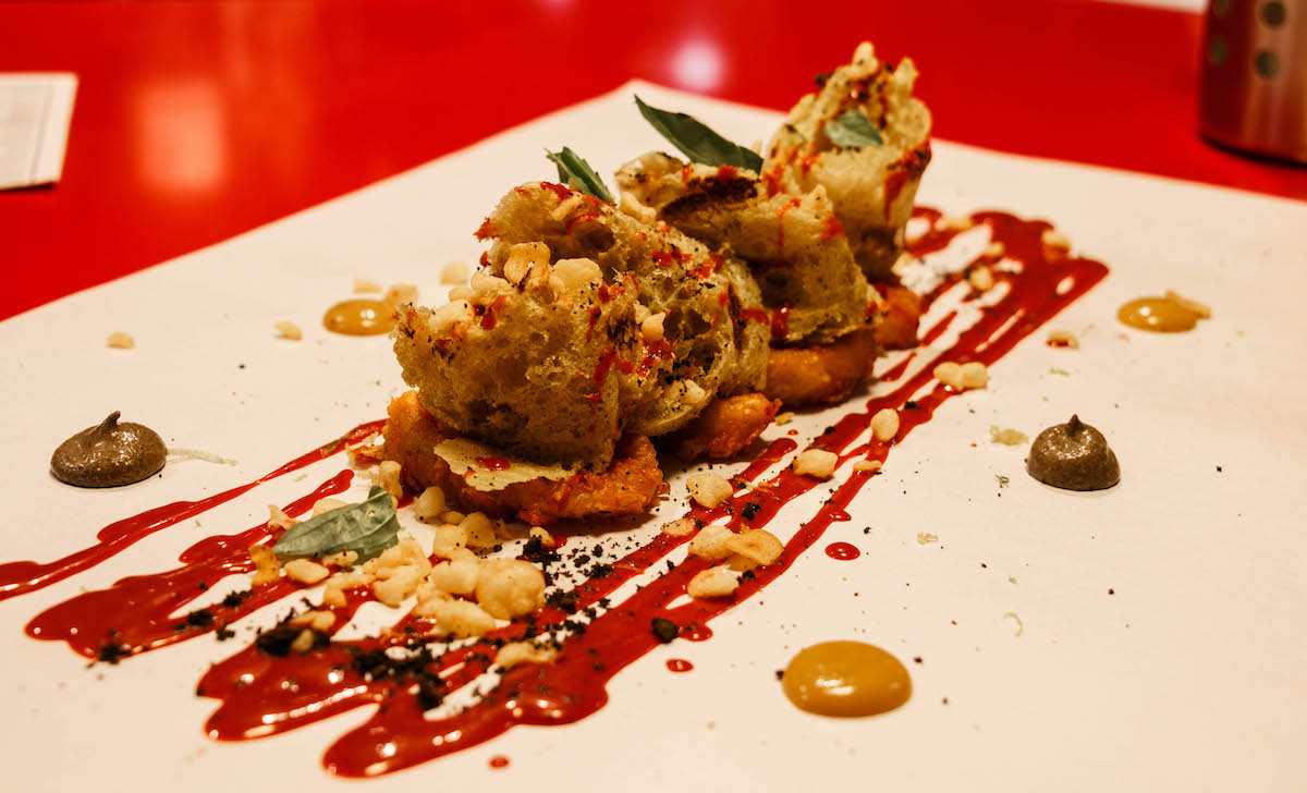 Una presentación moderna de anillos de calamares fritos y pequeños trozos de pan en un plato adornado con salsas